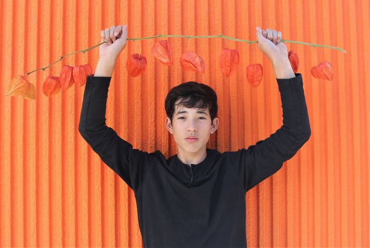 Portrait of boy holding leaves against orange wall