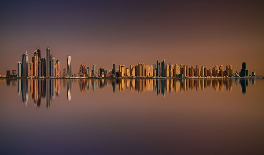 Reflection of buildings on lake against sky during sunset