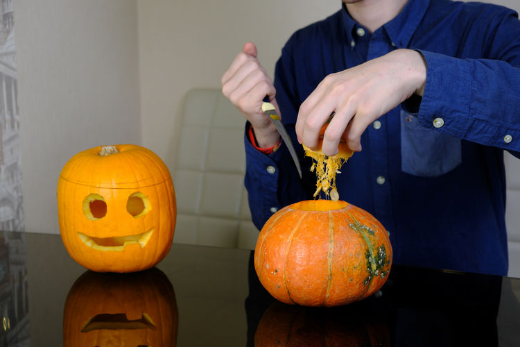 Midsection of man holding pumpkin against orange wall during halloween