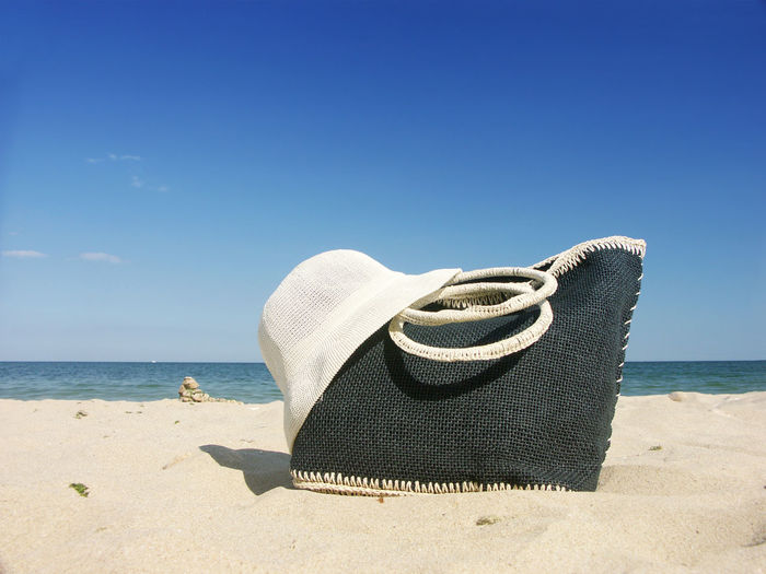 Beach bag with straw hat on a beach over sea and blue sky