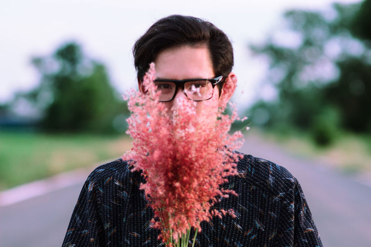 Portrait of man with coral flowers standing on road