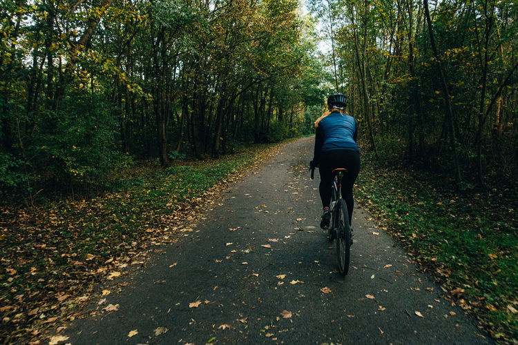 Rear view of woman riding bicycle on road amidst trees