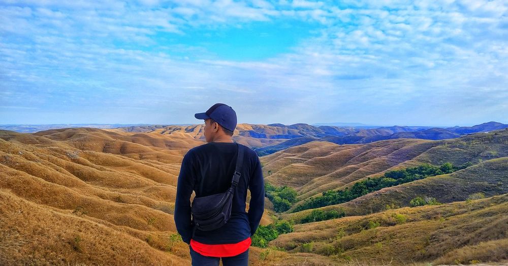 Rear view of man standing on mountain against sky