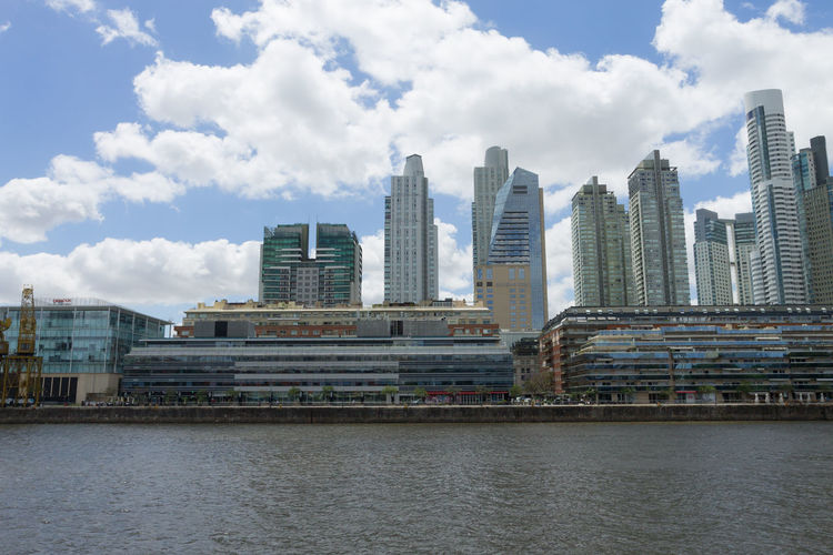 Modern buildings by river against sky in city