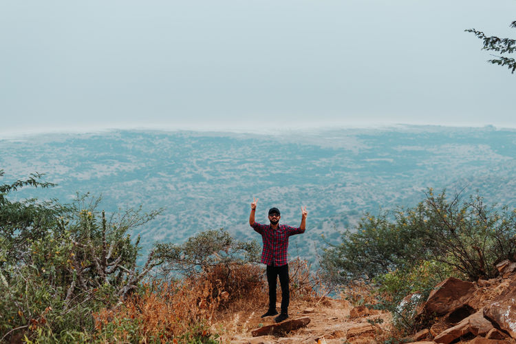 Portrait of man gesturing while standing on mountain against sky