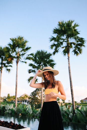 Smiling young woman standing against palm trees