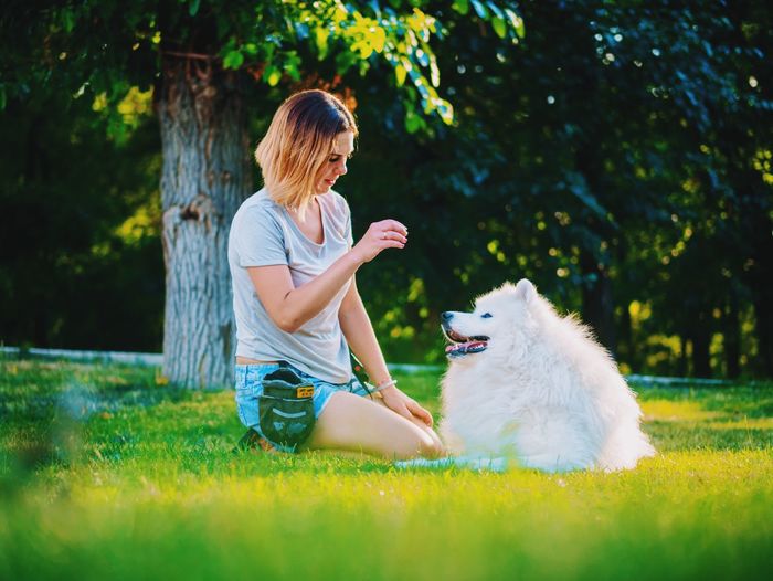 Woman playing with dog while kneeling on grassy field at back yard