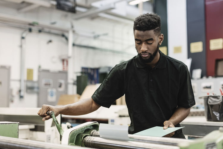 Young male student operating machine in workshop