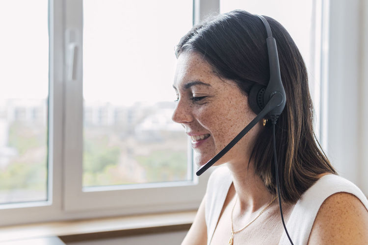 Happy young customer service representative with freckles on face wearing headset in office