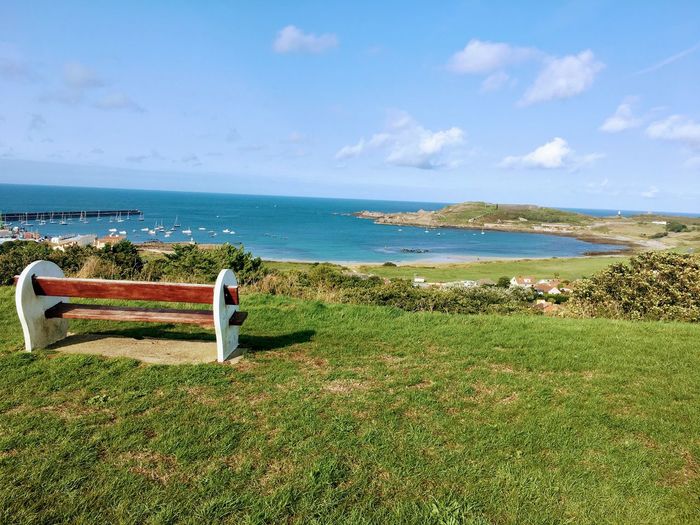 View of bench on beach against sky in alderney