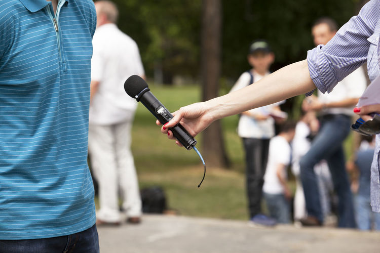 Cropped hand of woman holding microphone in front of man