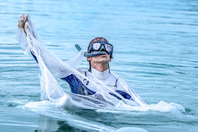 Mature man wearing scuba mask tearing plastic in sea