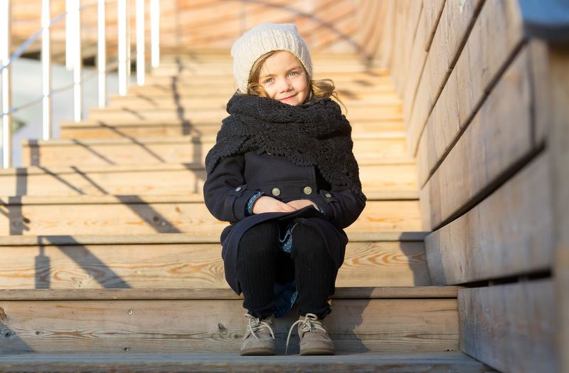 A five-year-old girl sits on wooden steps.