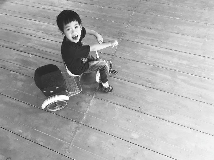 High angle portrait of boy cycling tricycle on hardwood floor