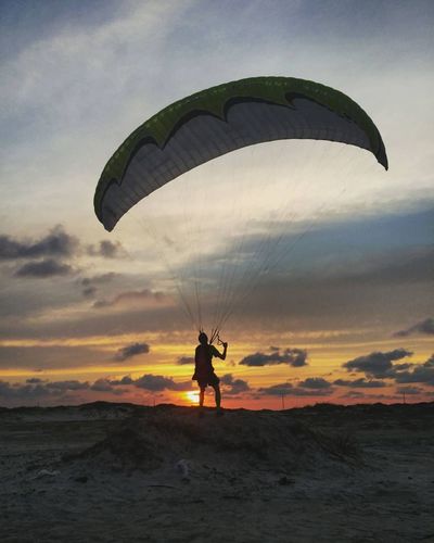 Rear view of man standing with parachute against orange sky