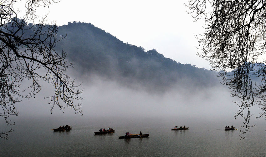 High angle view of people in rowboats on lake amidst fog 