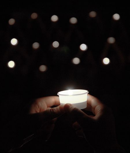 Close-up of hand holding candles in white plastic cup of lighting equipment