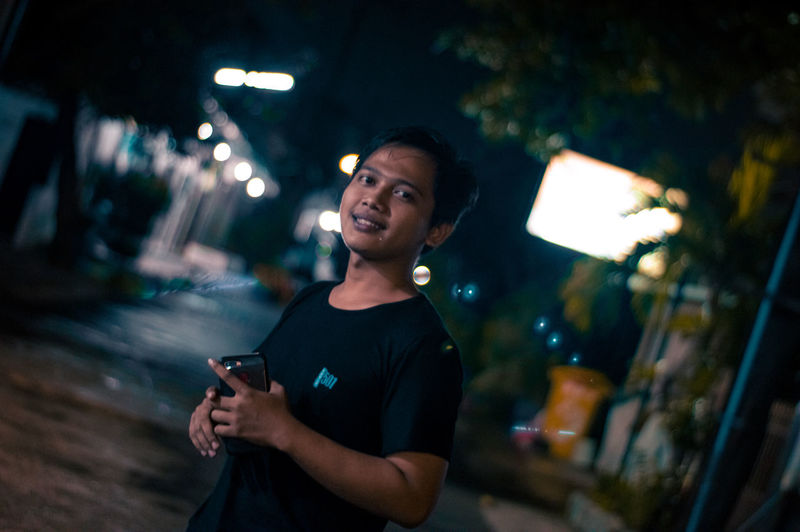 Young man using mobile phone in city at night