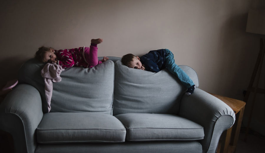 Playful siblings lying on sofa at home