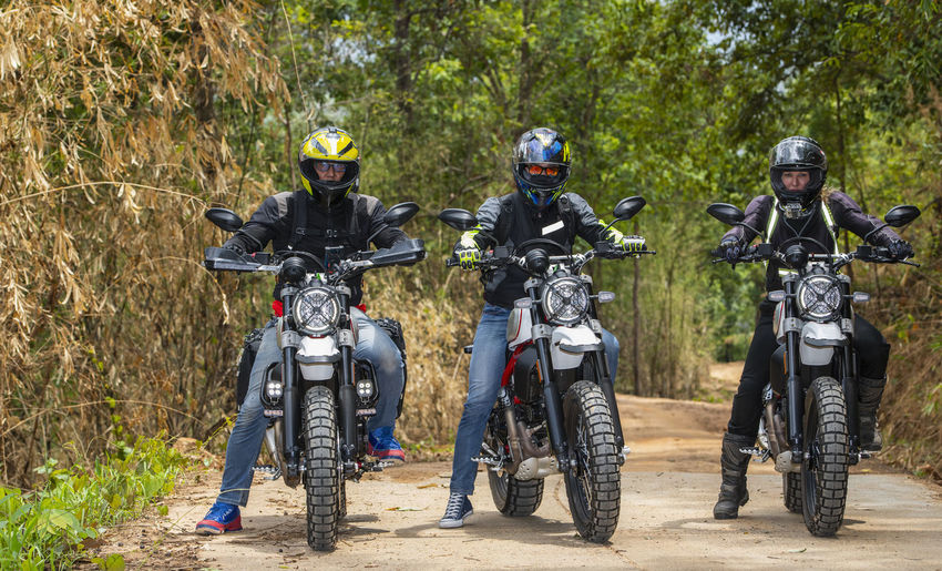 Three friends riding their scrambler motorcycles through forrest