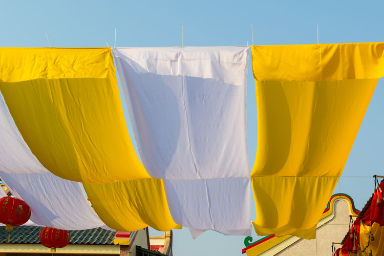 Yellow and white fabrics hanging against sky