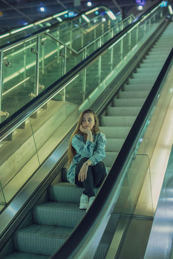 Young woman looking away while sitting on escalator