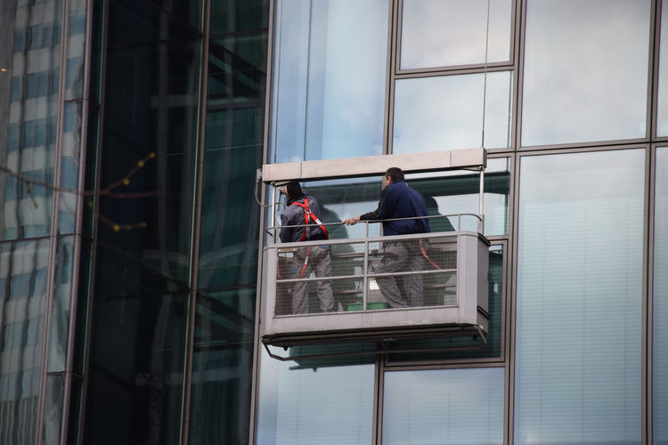 Low angle view of window washers cleaning glass building