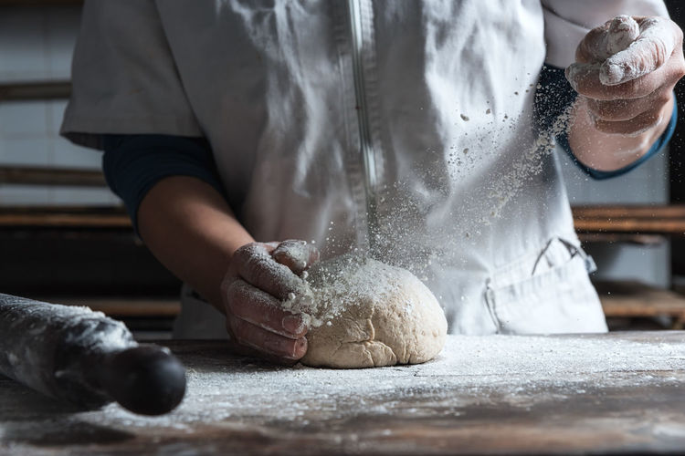 Unrecognizable person kneading dough with flour on table while working in bakery