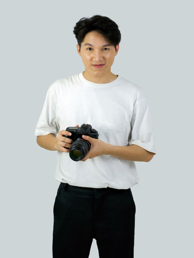 Portrait of young man photographing against white background