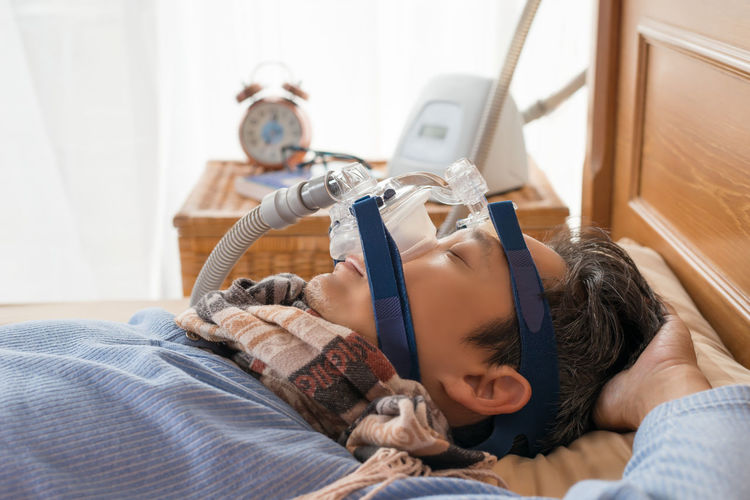 Mature man wearing oxygen mask while sleeping on bed