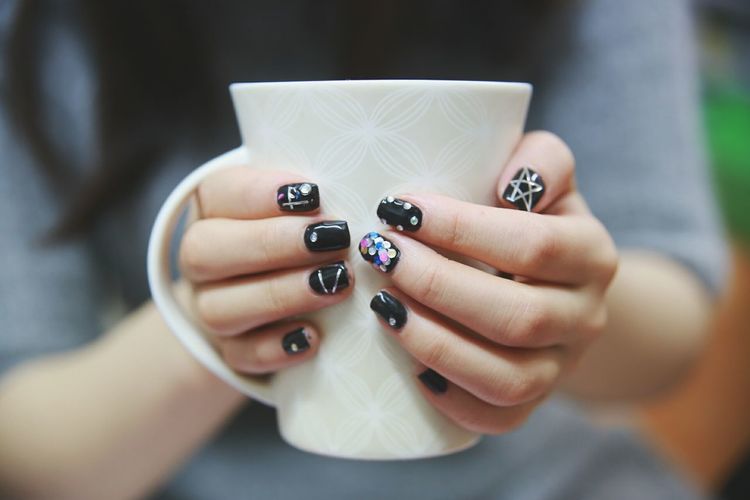 Midsection of woman with nail art holding cup