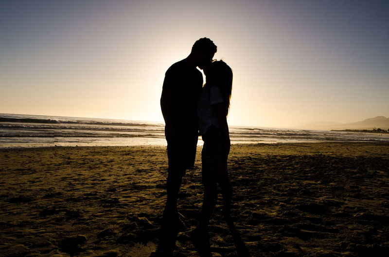 Silhouette woman kissing man against sea during sunset