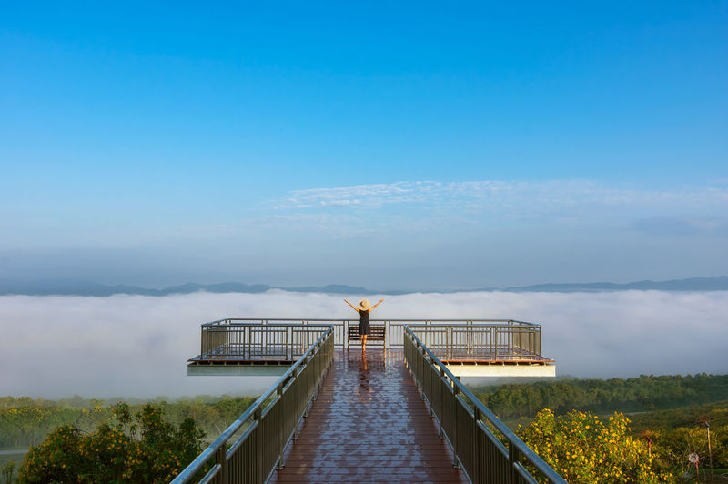 Rear view of woman standing by railing at observation point against cloudy sky