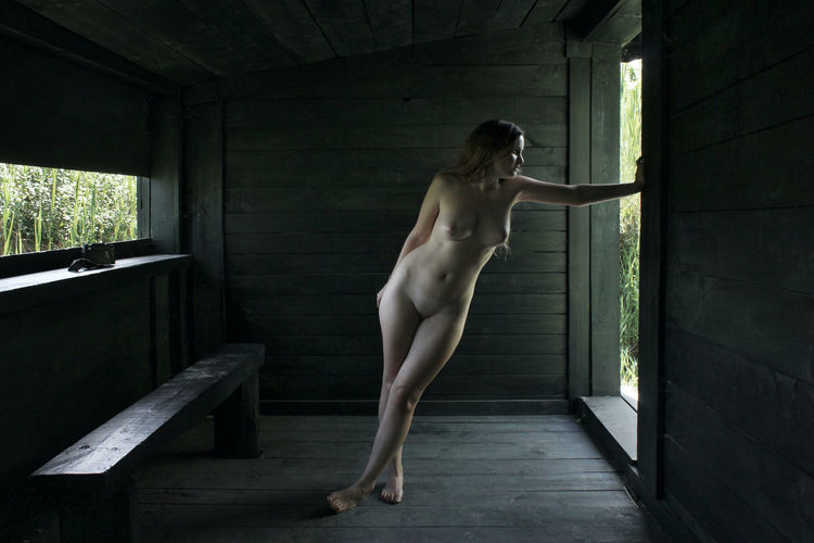 Full length of shirtless man standing against window