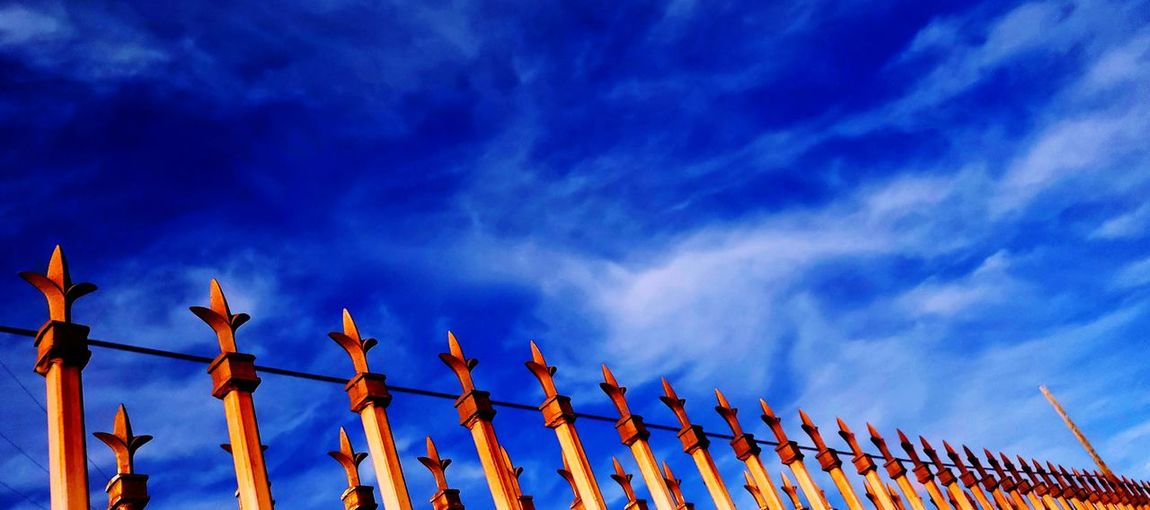 Low angle view of barbed wire fence against blue sky
