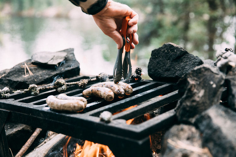 Cropped image of man roasting sausages on metal grate at campsite