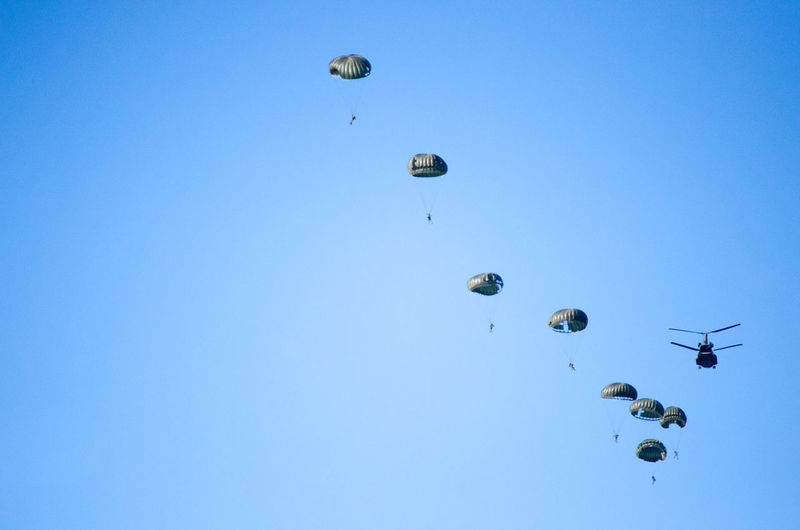 Low angle view of helicopter with parachutes in clear blue sky