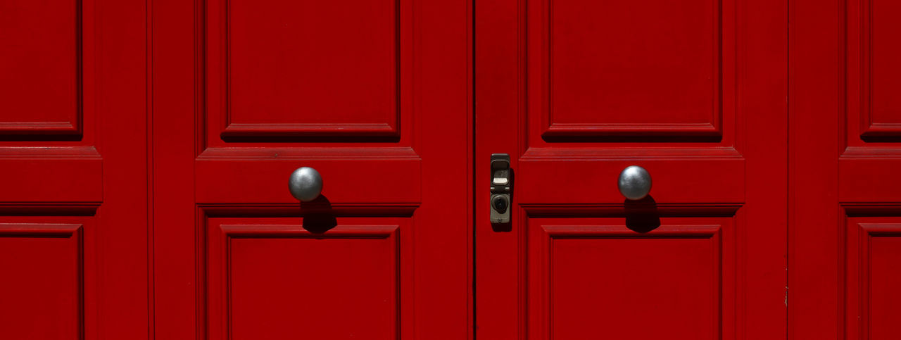Portion of door in red lacquered wood with metal knobs and lock.