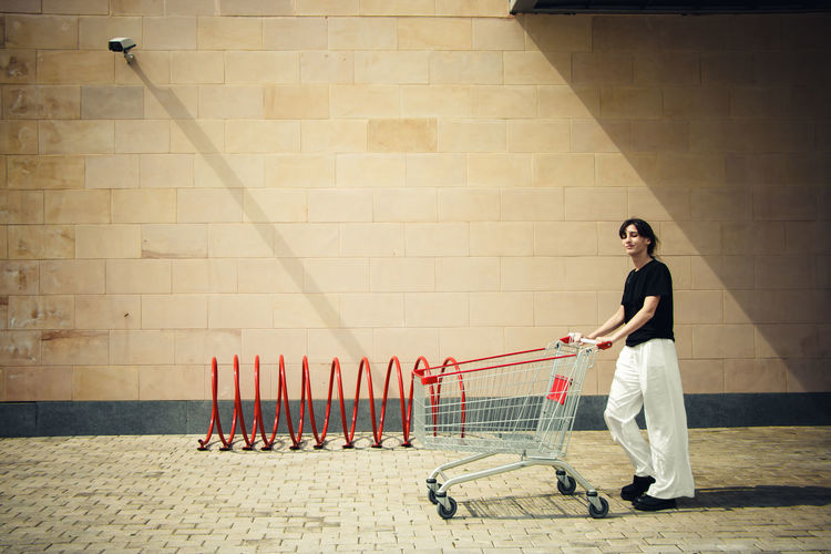 Full length of woman pushing shopping cart against wall