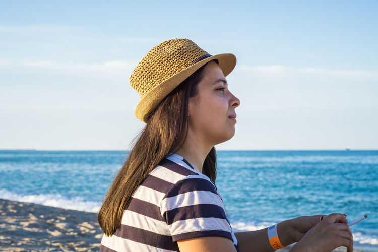 Woman in hat looking at sea against sky