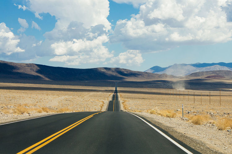 Empty desert road towards mountains against sky