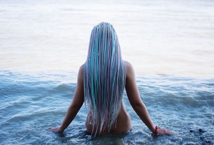 Rear view of naked woman with colorful long hair standing in sea