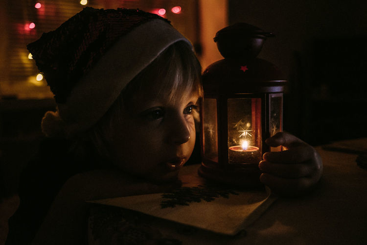 Portrait of child in santa's hat near candle in illuminated room at night 