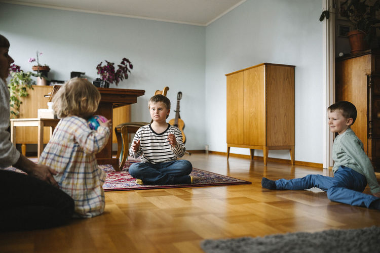 Full length of siblings sitting on floor at home