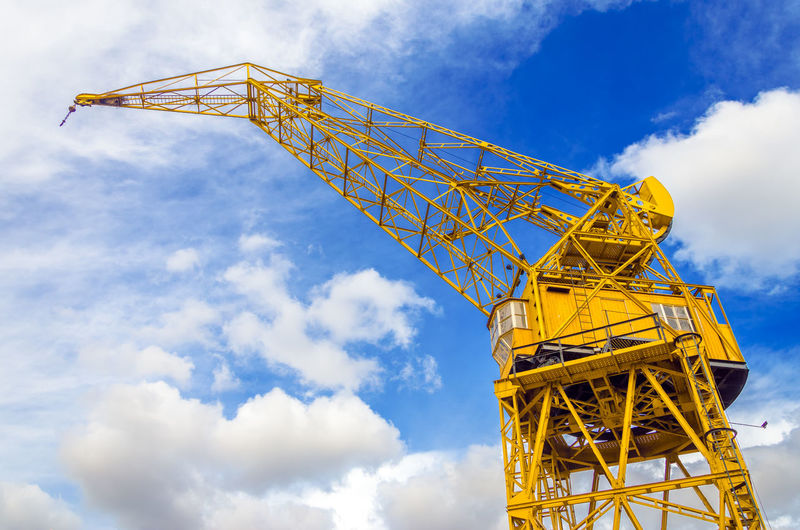 Low angle view of yellow crane against cloudy sky