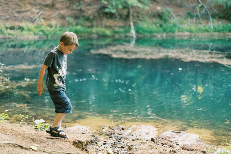 A five year old boy playing by a turquoise pond in the woods