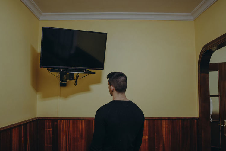 Rear view of man standing against wall at home
