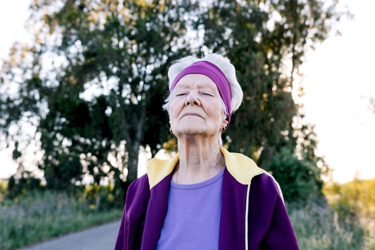 Elderly female athlete with closed eyes breathing fresh air during fitness training in countryside
