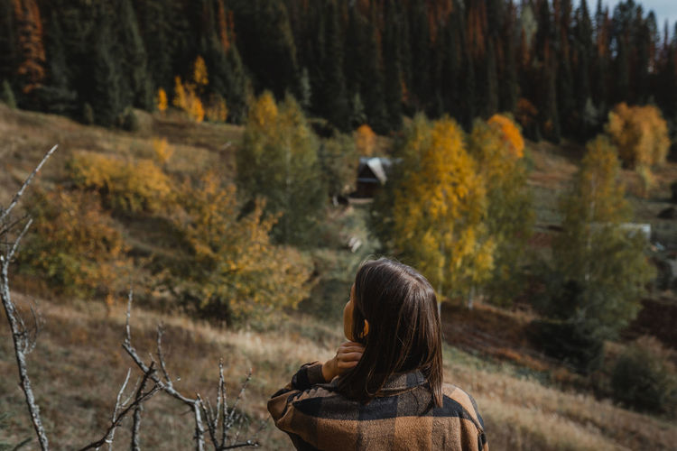 Rear view of woman standing amidst trees in forest during autumn
