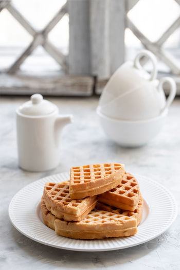 Waffles with yogurt on a white porcelain plate with black geyser coffee maker on the windowsill